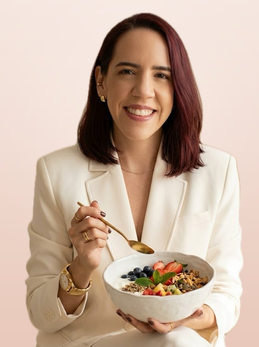 Alessandra Macedo de terno claro, sorrindo e segurando uma tigela com iogurte, frutas e granola